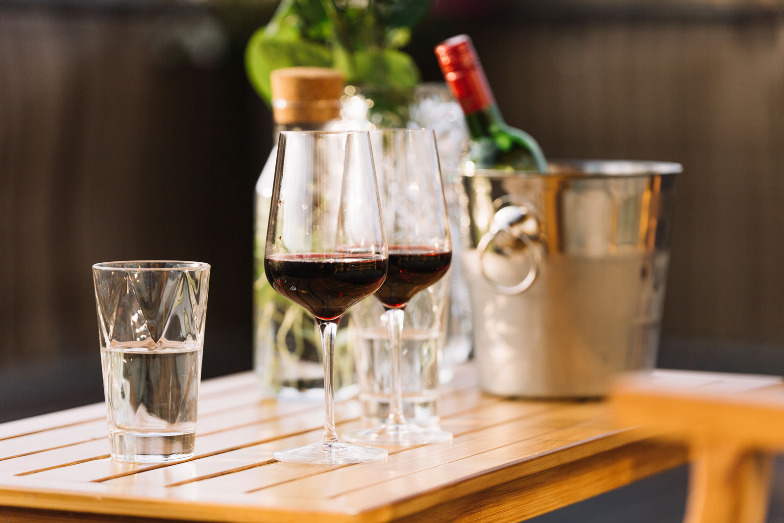 Two glasses of red wine on a table on the foreground. On the background we can see an ice bucket with a red wine bottle.